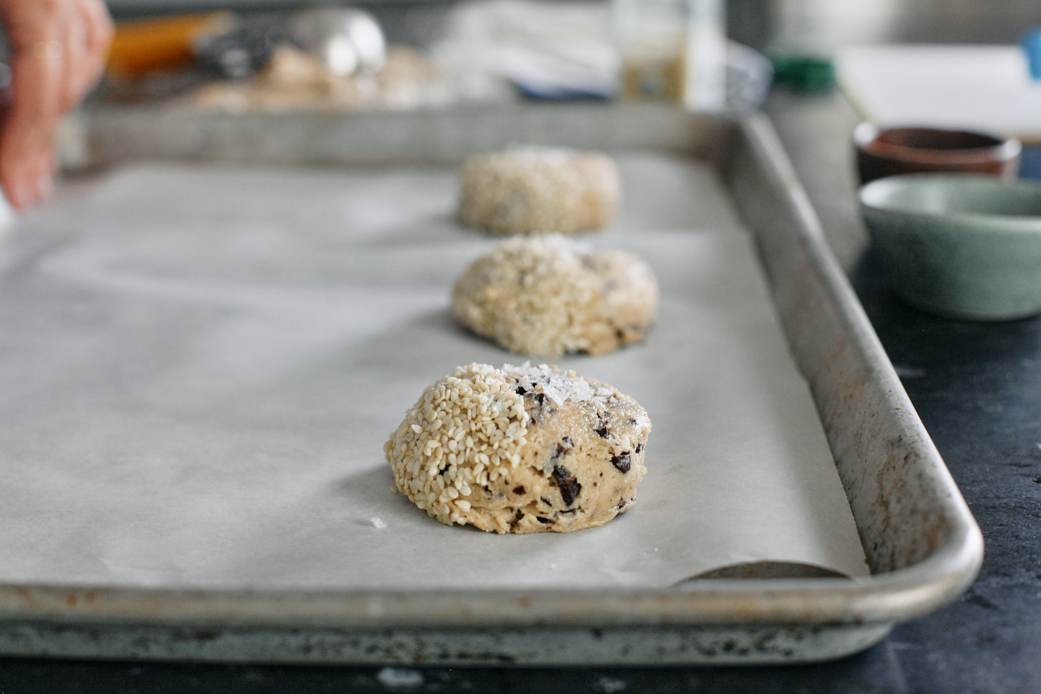 Halva Chocolate Chip Cookies 3 halva chocolate chip cookie dough scooped and placed on a a parchment lined cookie sheet, half topped with sesame seeds and half topped with flaky sea salt