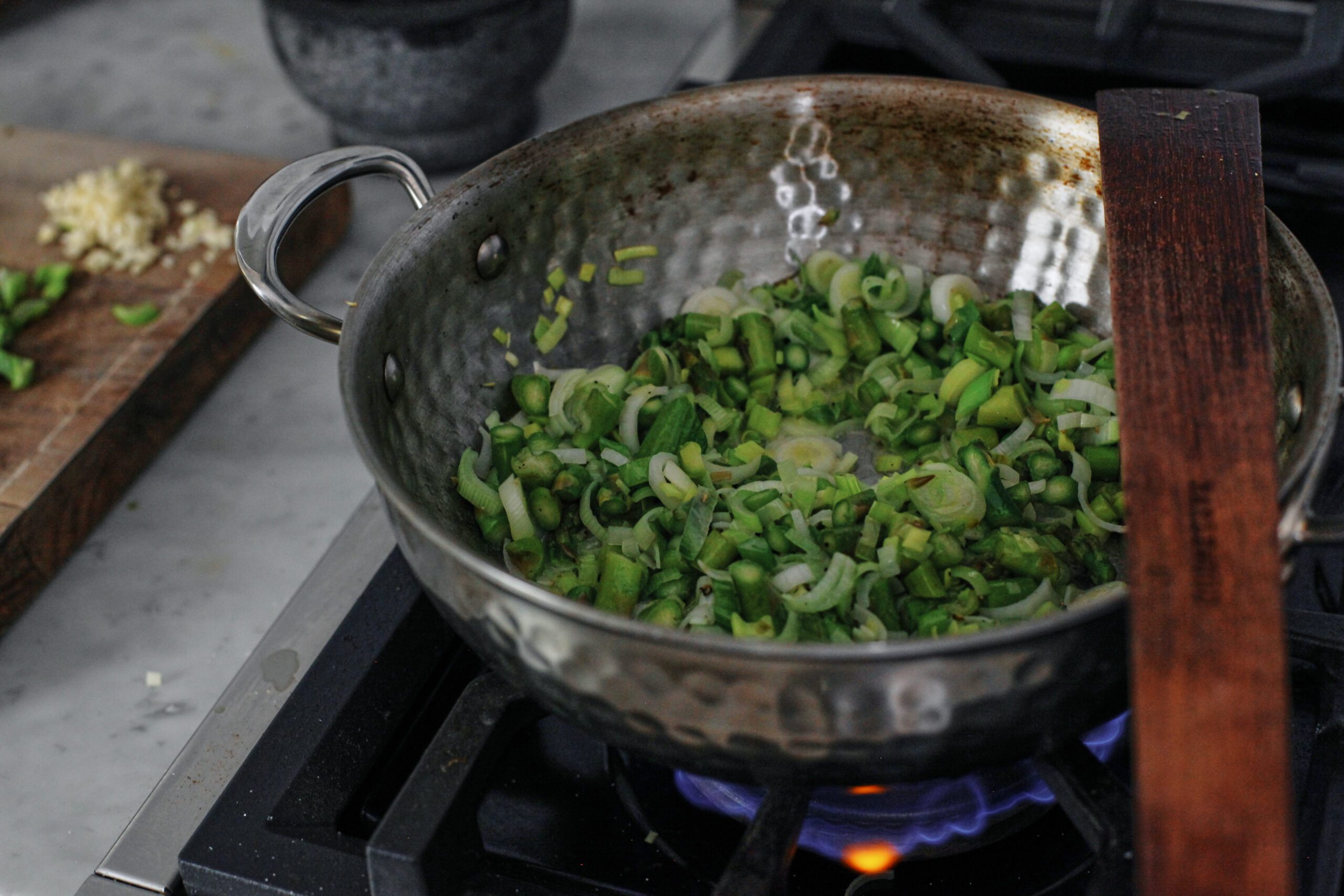 green onion, leek, asparagus being sautéed in a pan over a gas stove