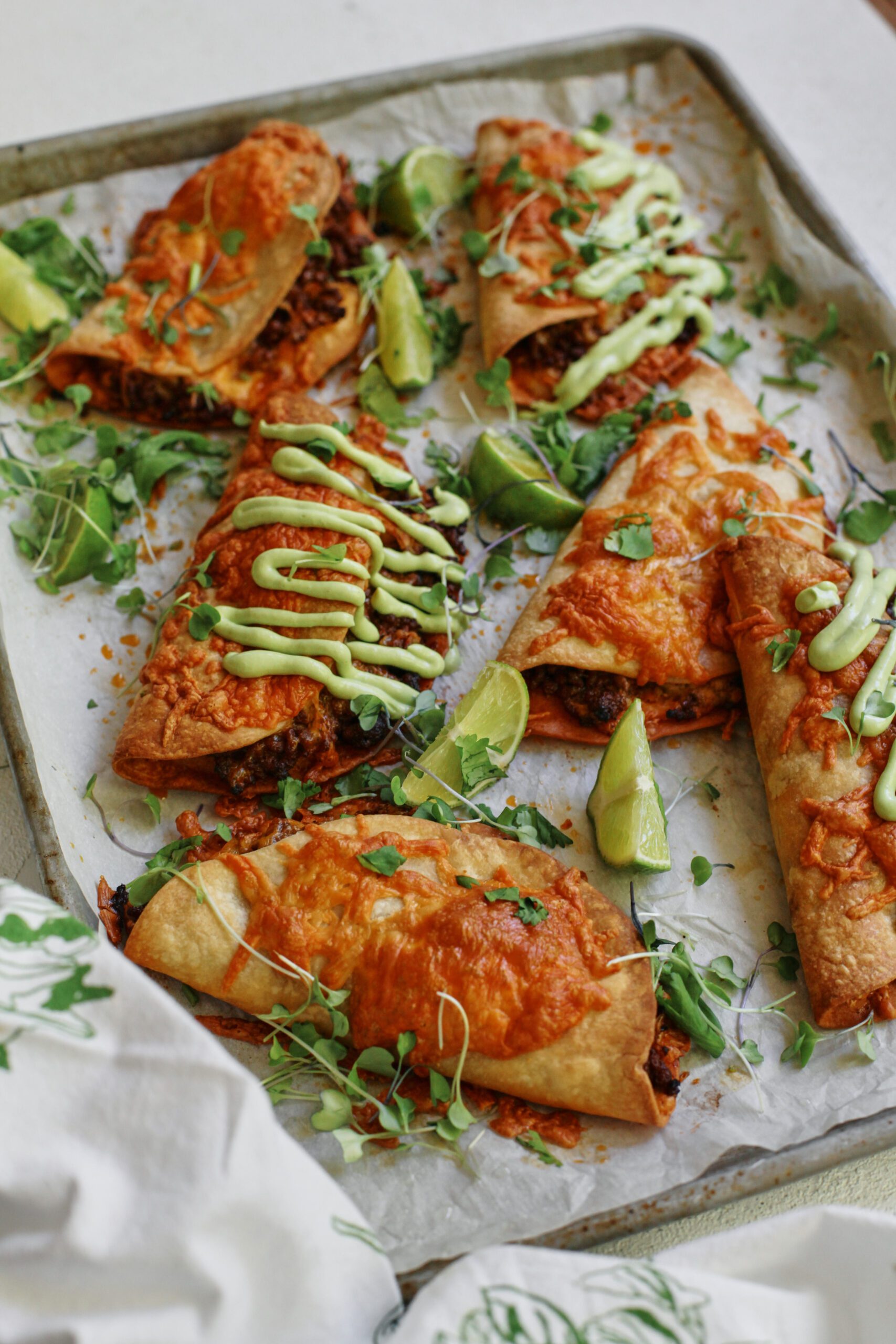 sheet pan beef tacos dressed with avocado lime crema, cilantro, and lime wedges
