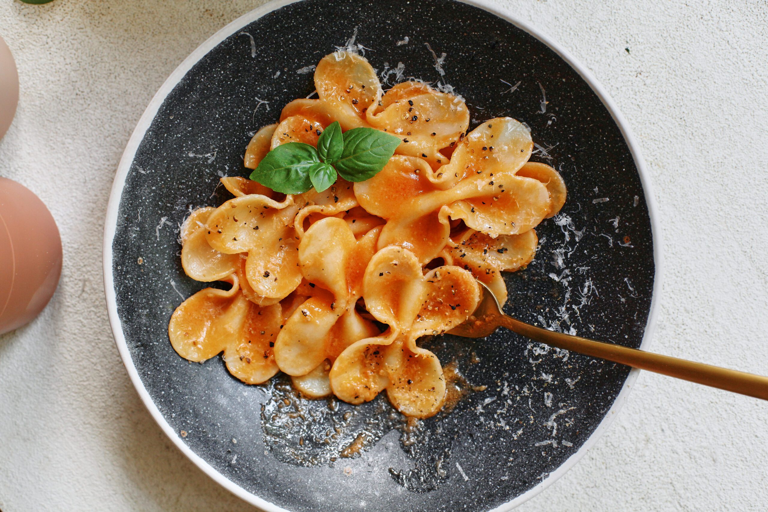 single serve tomato pasta garnished with parmesan and basil, fork in the bowl