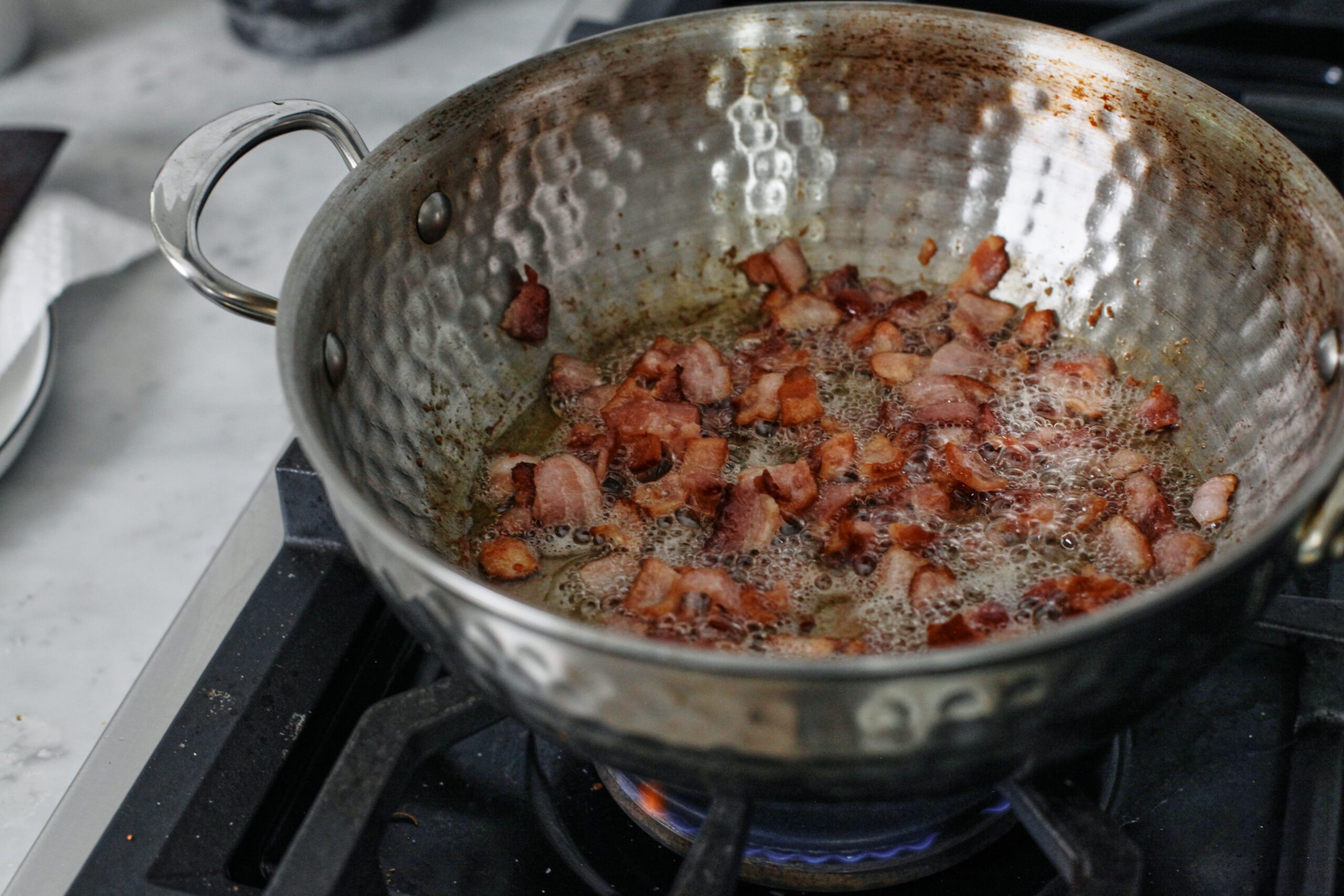 Chopped bacon cooking in a pot on the stove