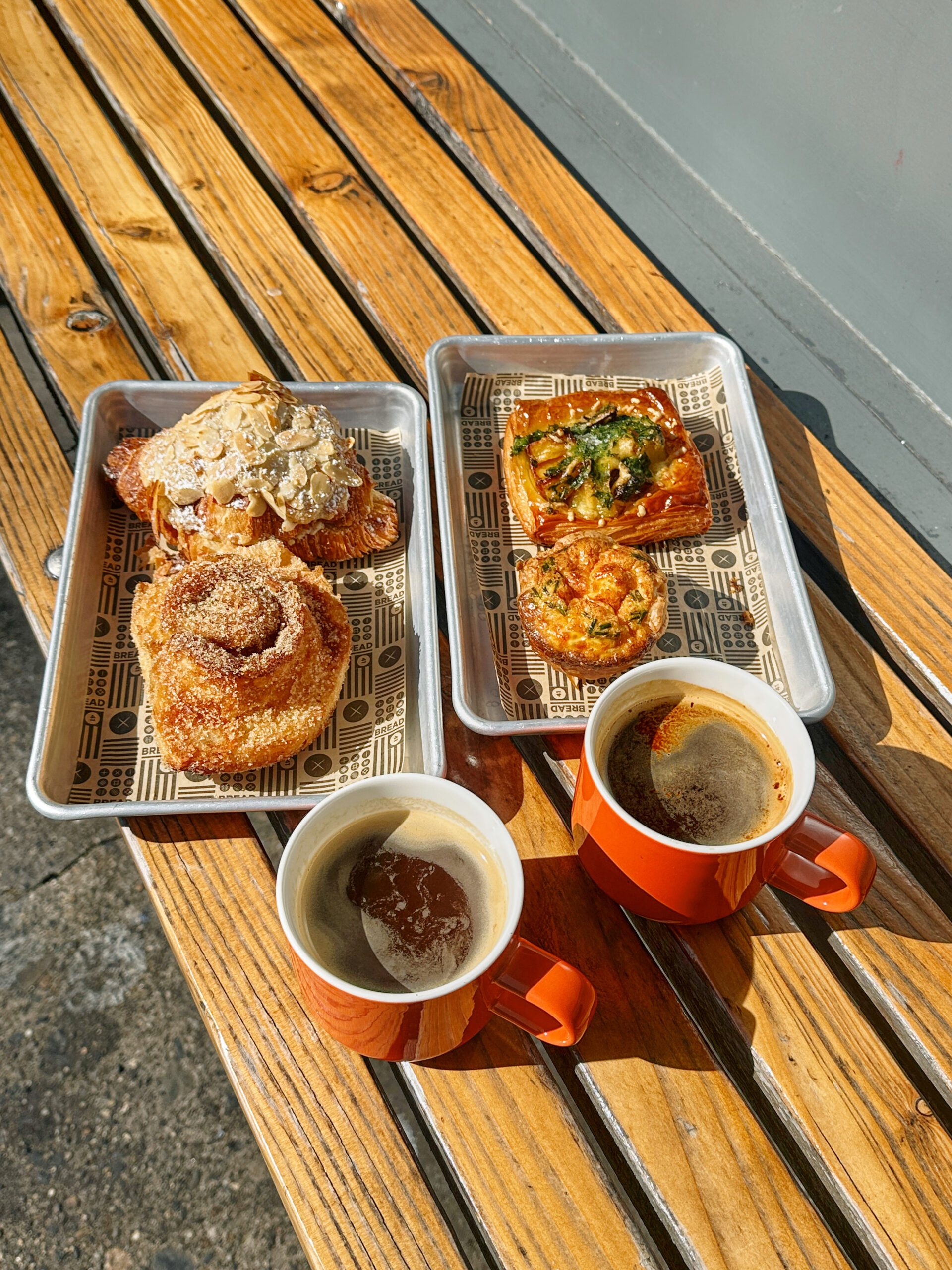 two trays with pastries on them and two mugs of coffee