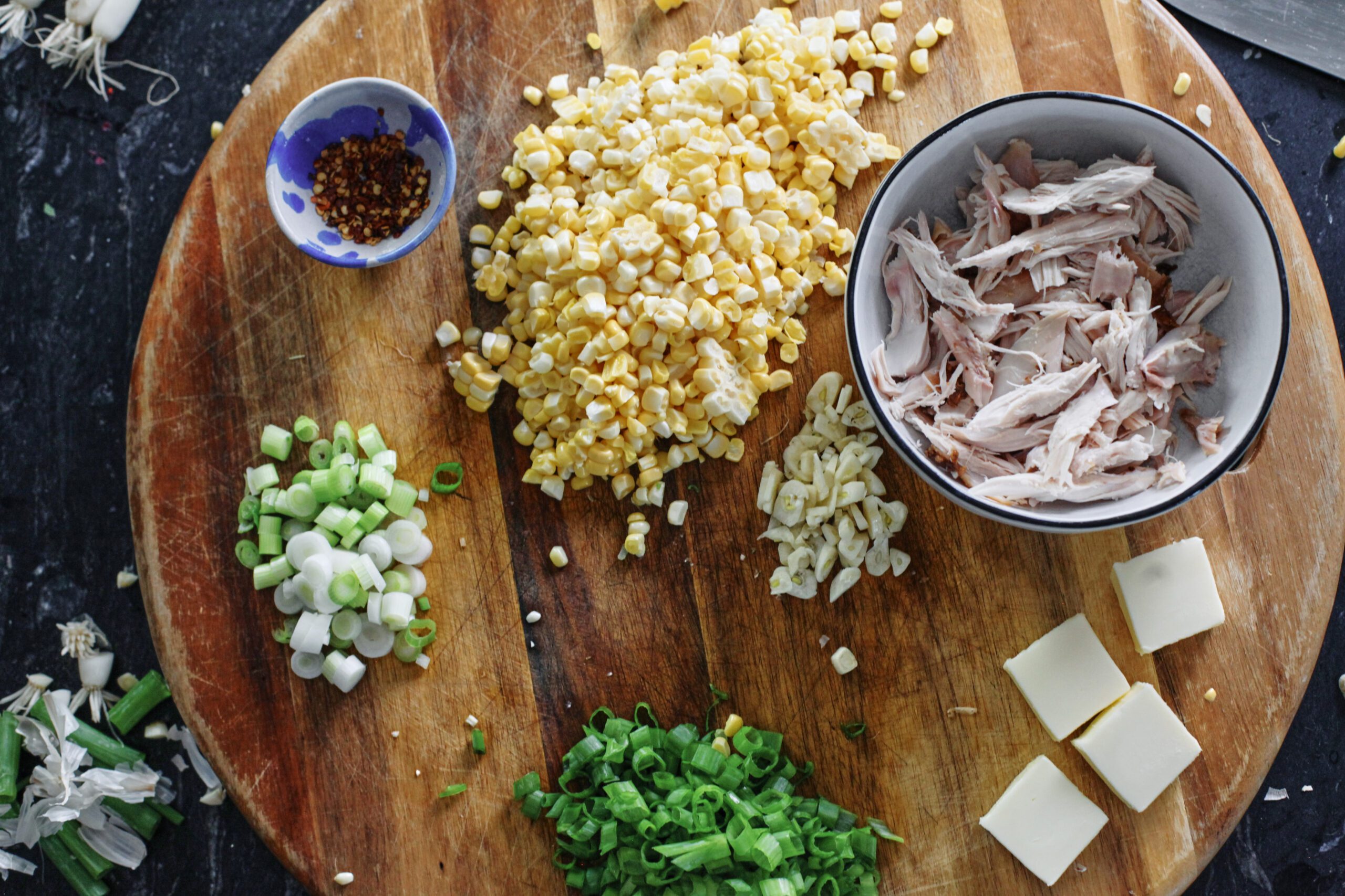Creamy Corn and Chicken Pasta 5 prepped ingredients for creamy corn and chicken pasta: red chili flakes, corn, rotisserie chicken, sliced garlic, butter, green onions