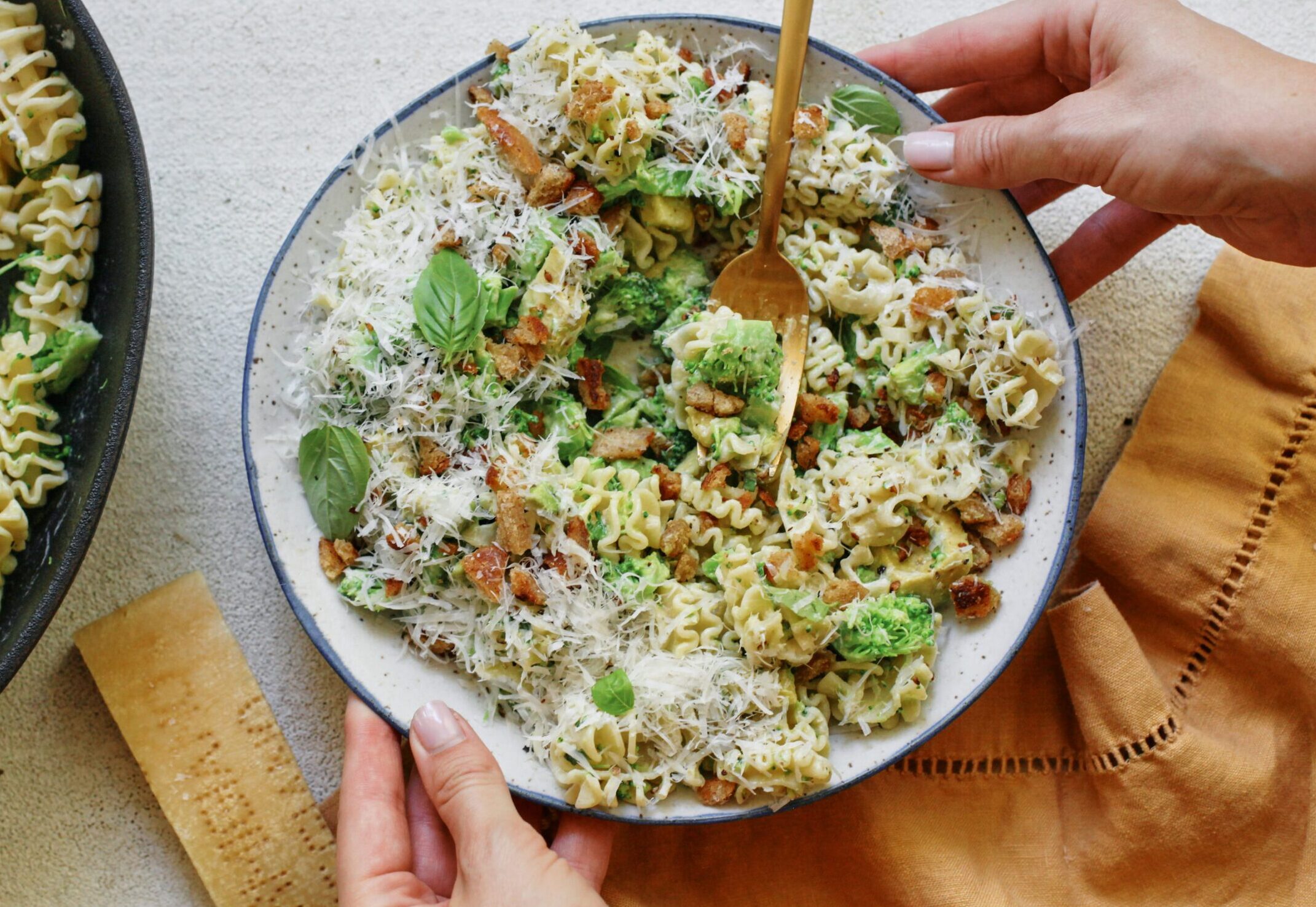 two hands placing a bowl of broccoli caesar pasta salad down on the table