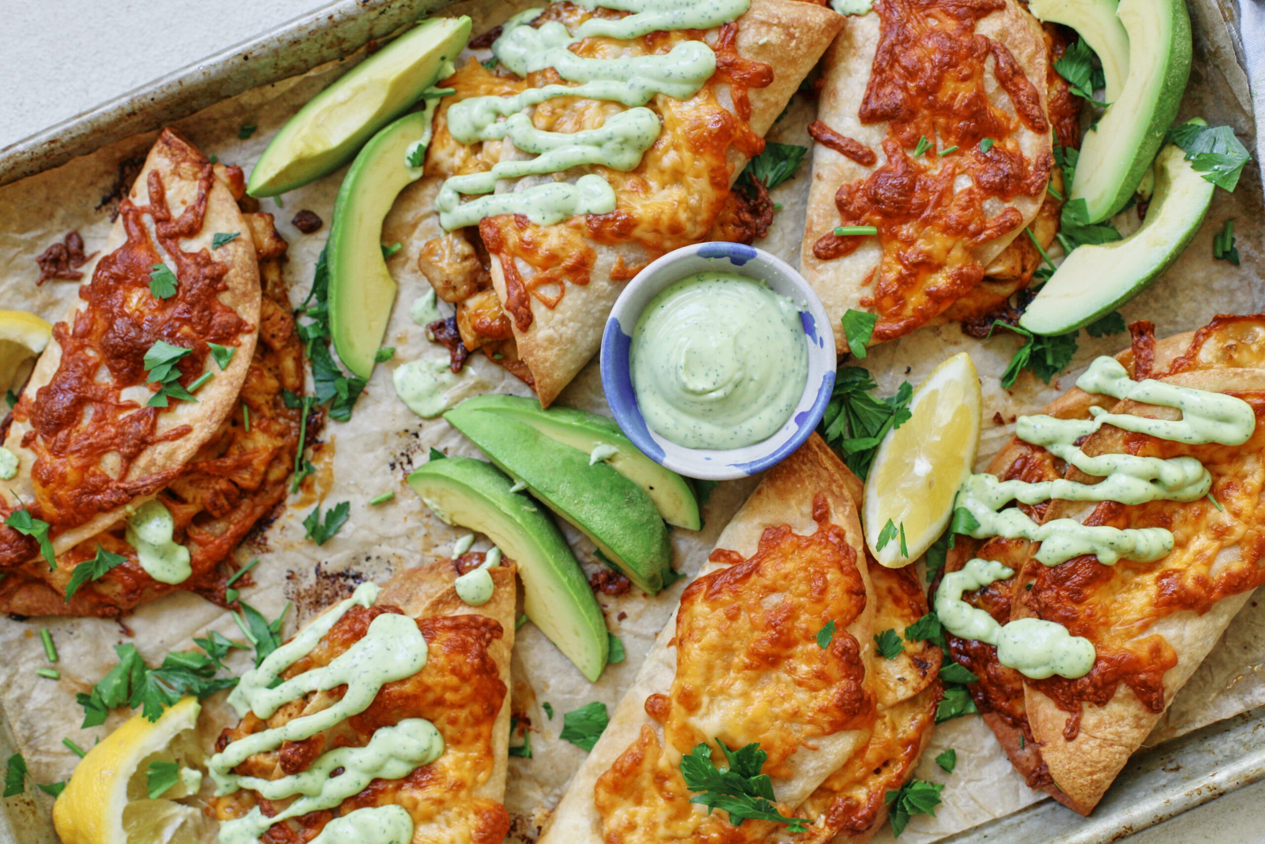 crispy chicken sheet pan tacos with a green goddess ranch on a baking tray - garnished with avocado and lemon