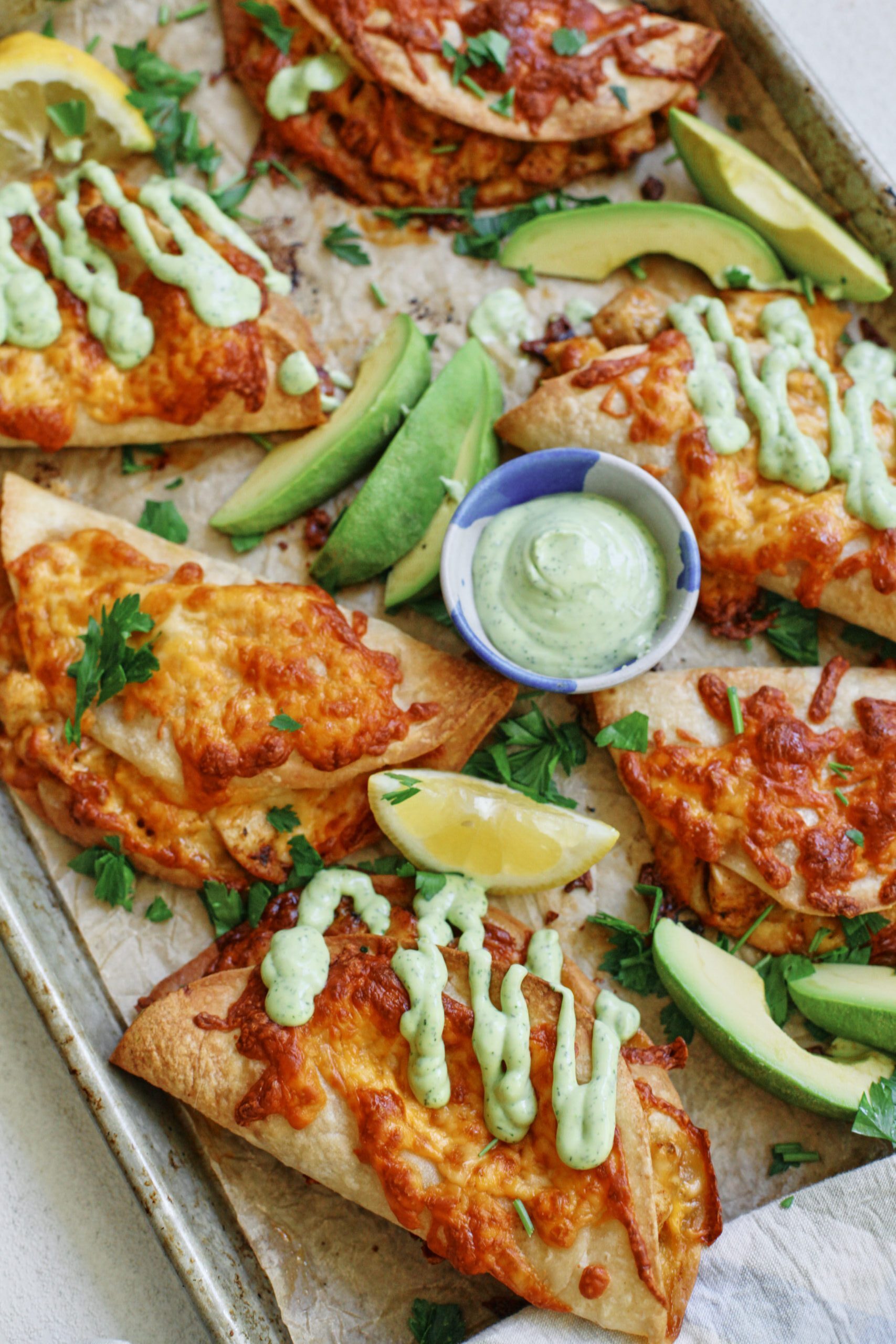 crispy chicken sheet pan tacos with a green goddess ranch on a baking tray - garnished with avocado and lemon
