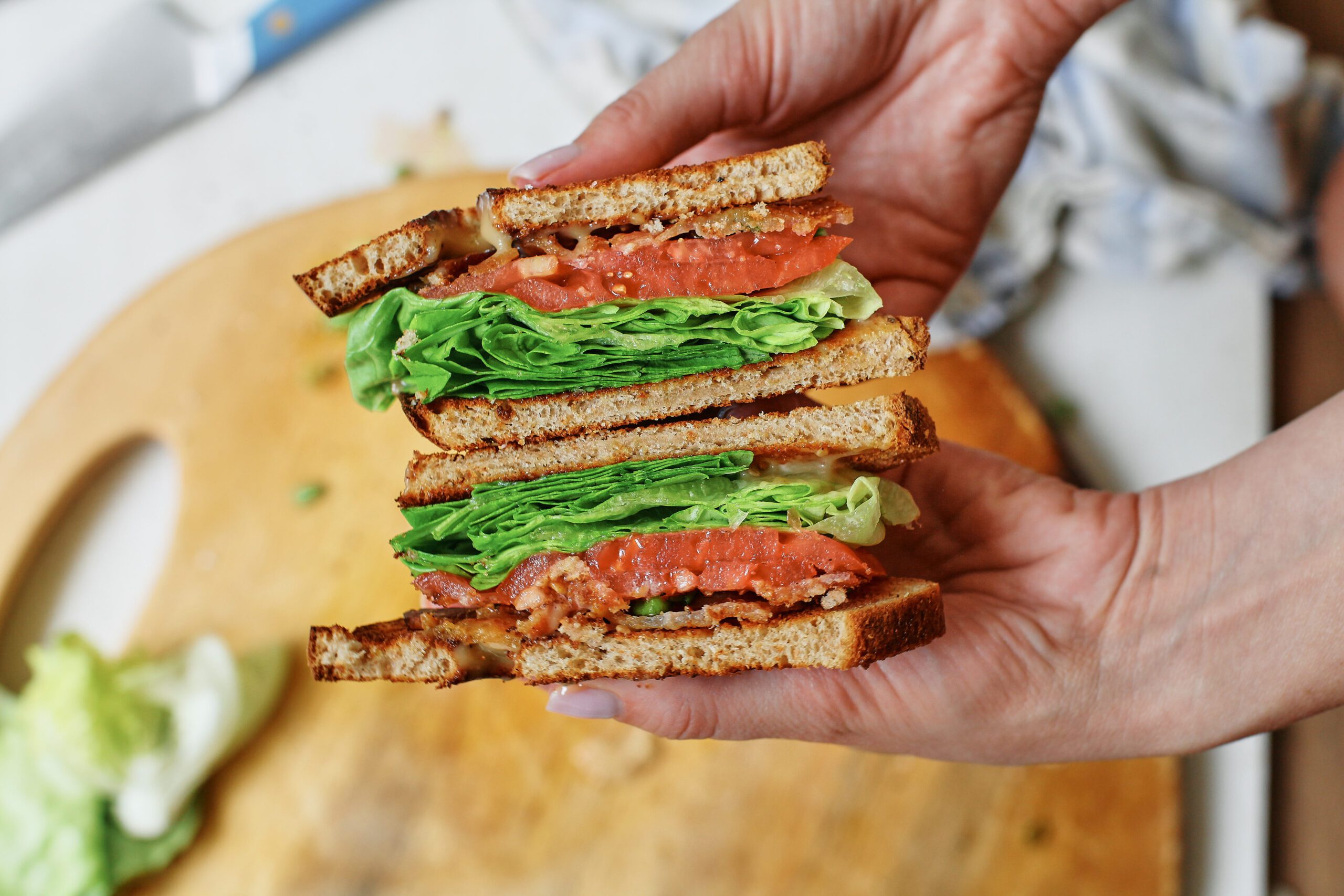 two halves of a BLT sandwich stacked together and being held in between hands