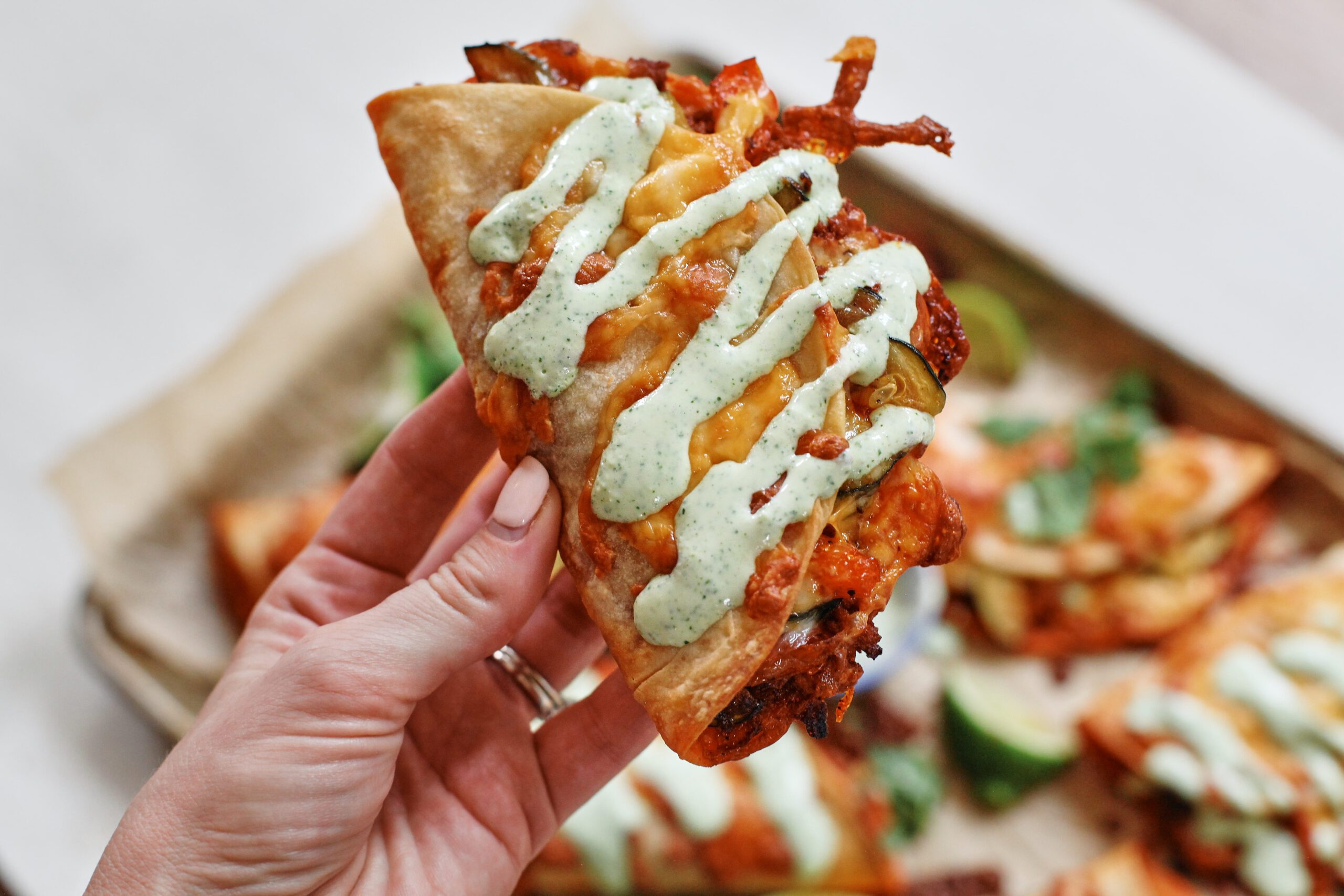 a hand holding a taco with jalapeño garlic crema drizzled on it