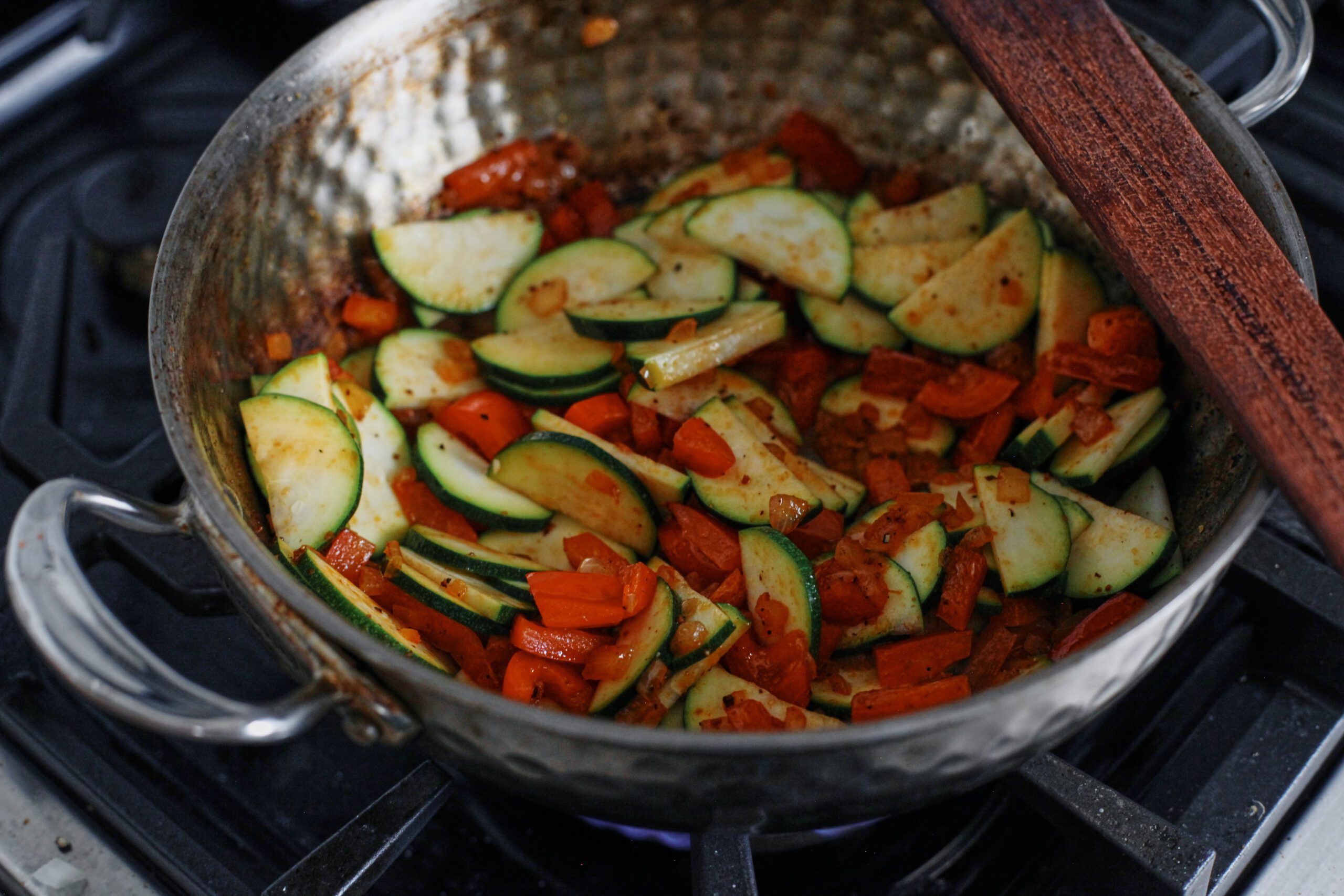 chopped red bell peppers + zucchini sautéing in a pan on the stove