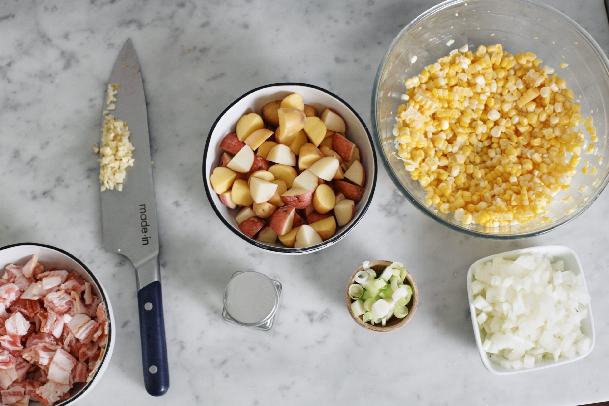 prepped ingredients for creamy corn chowder: chopped bacon, green onions, corn, potatoes, minced garlic, onion