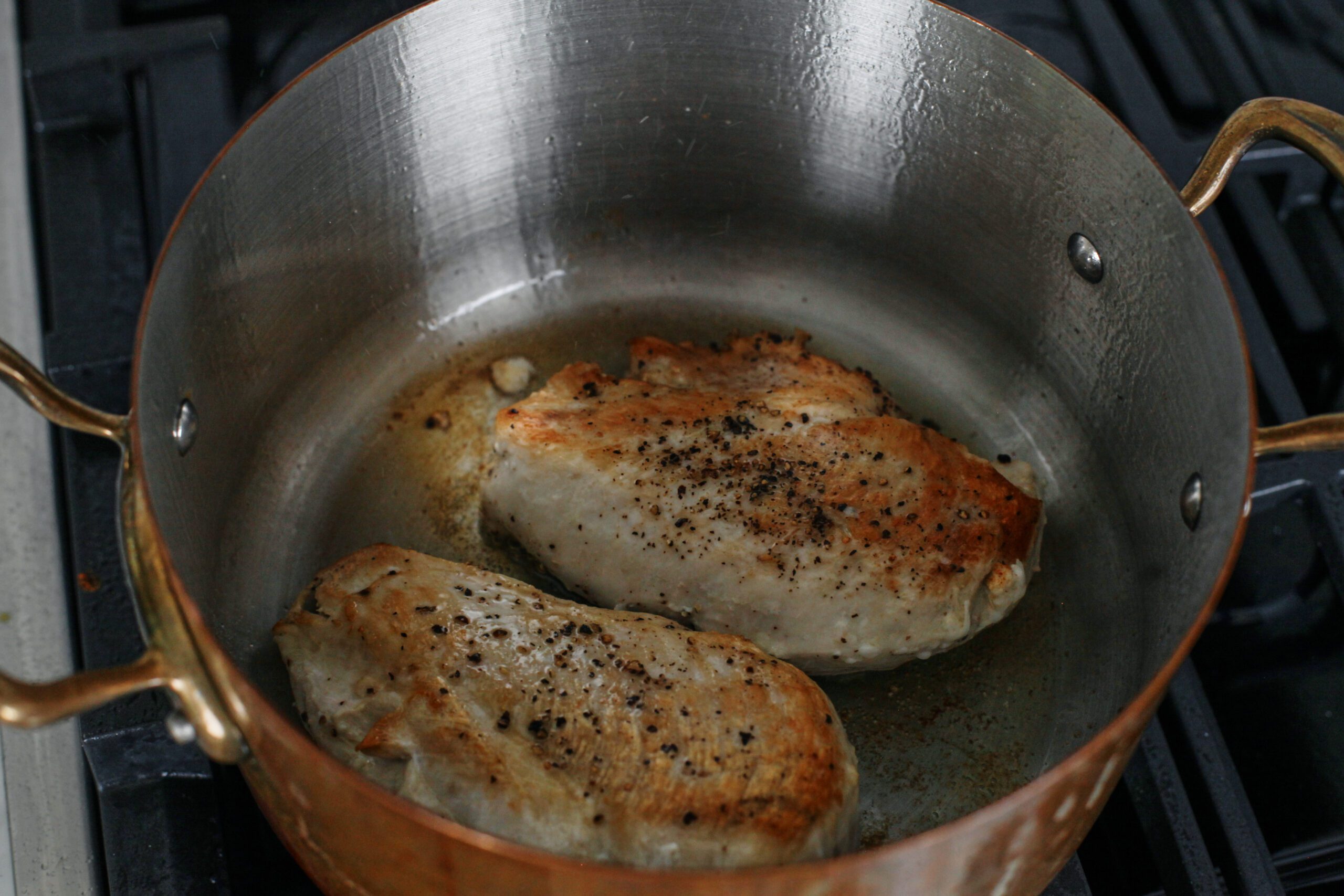 two chicken breasts searing in a pot