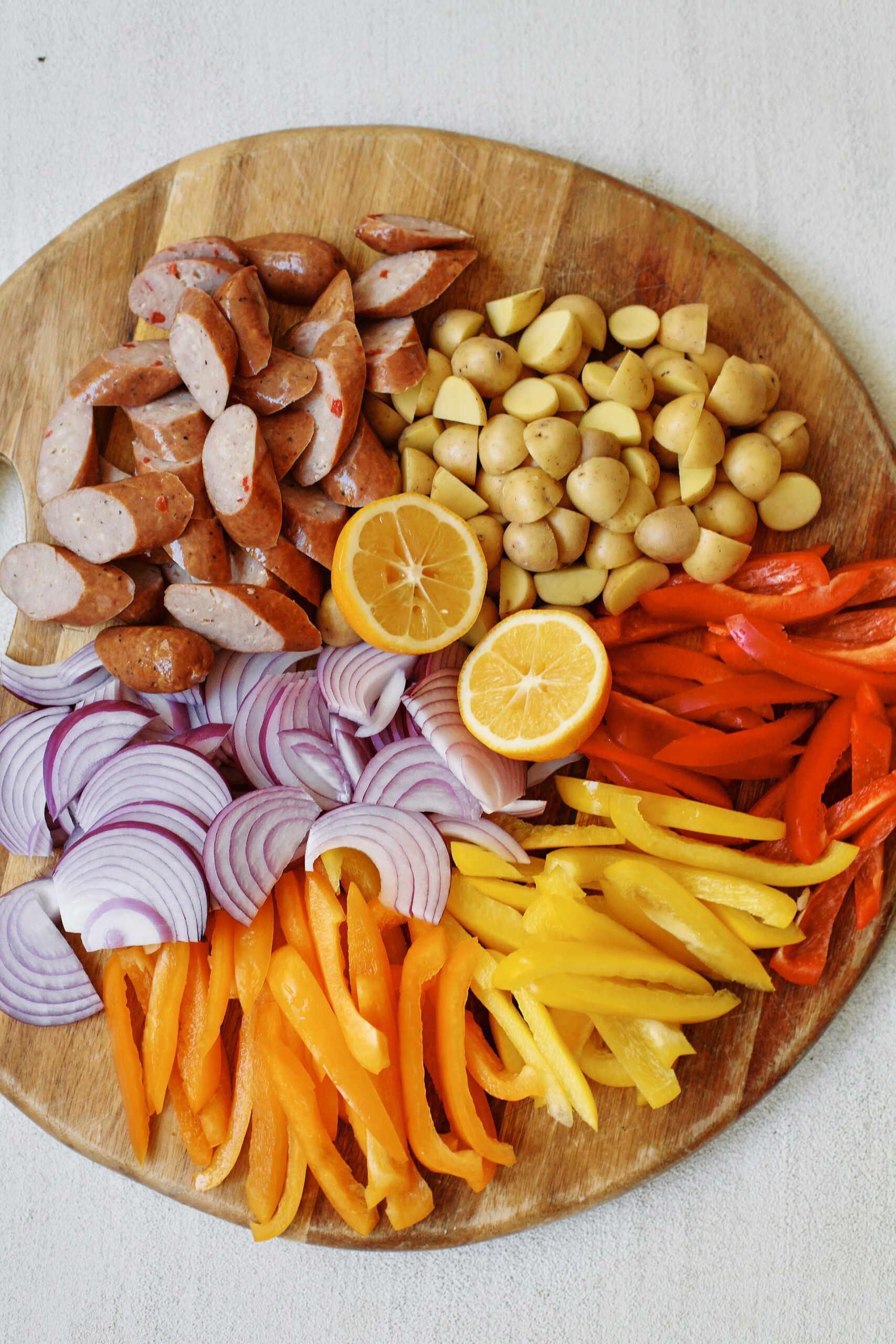 prepped ingredients: chopped sausages, red onion, orange, yellow, and red bell peppers, baby potatoes, and a lemon