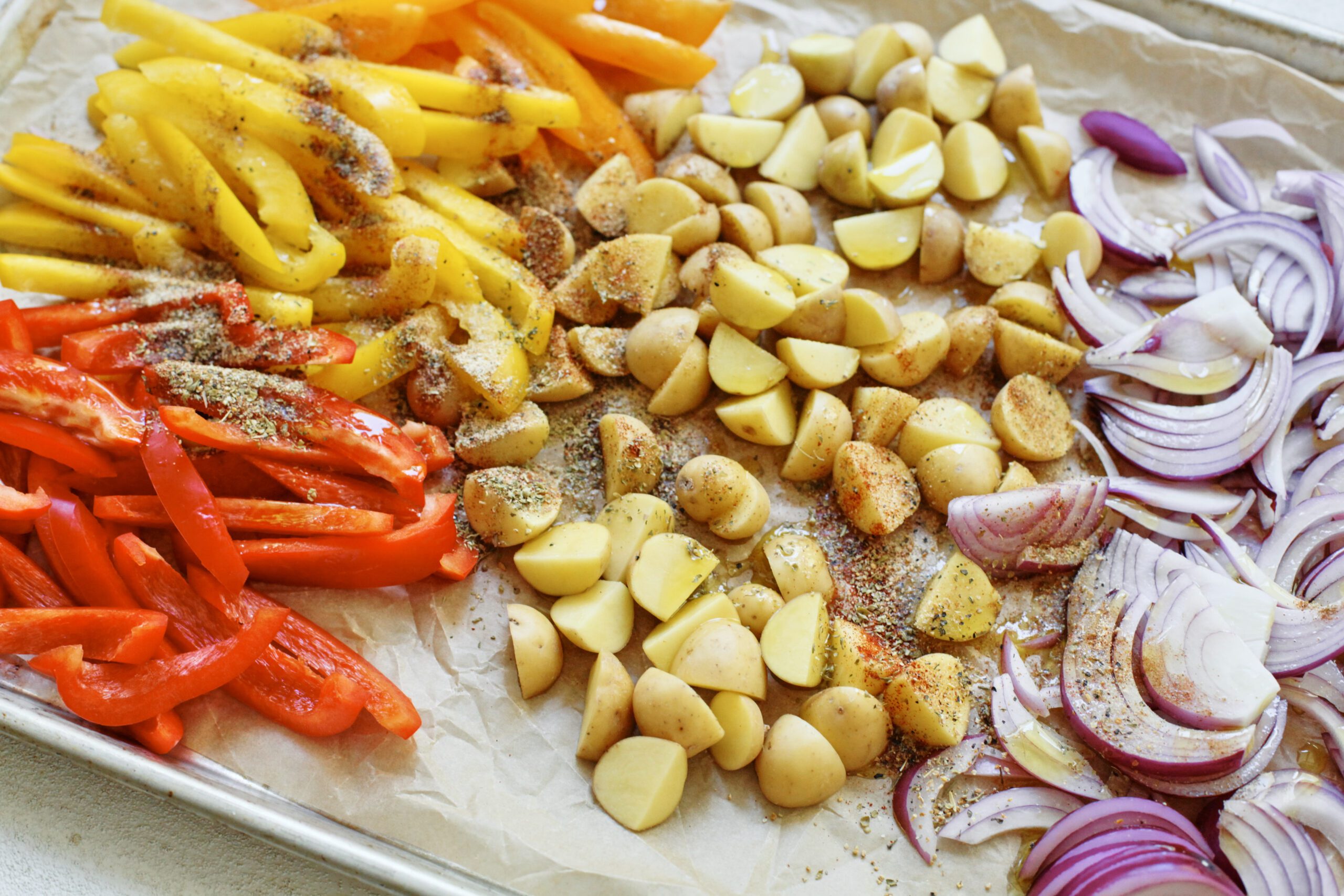 Sheet Pan Sausage, Peppers & Potatoes 2 peppers, potatoes, and onions on a sheet pan ready to roast in the oven