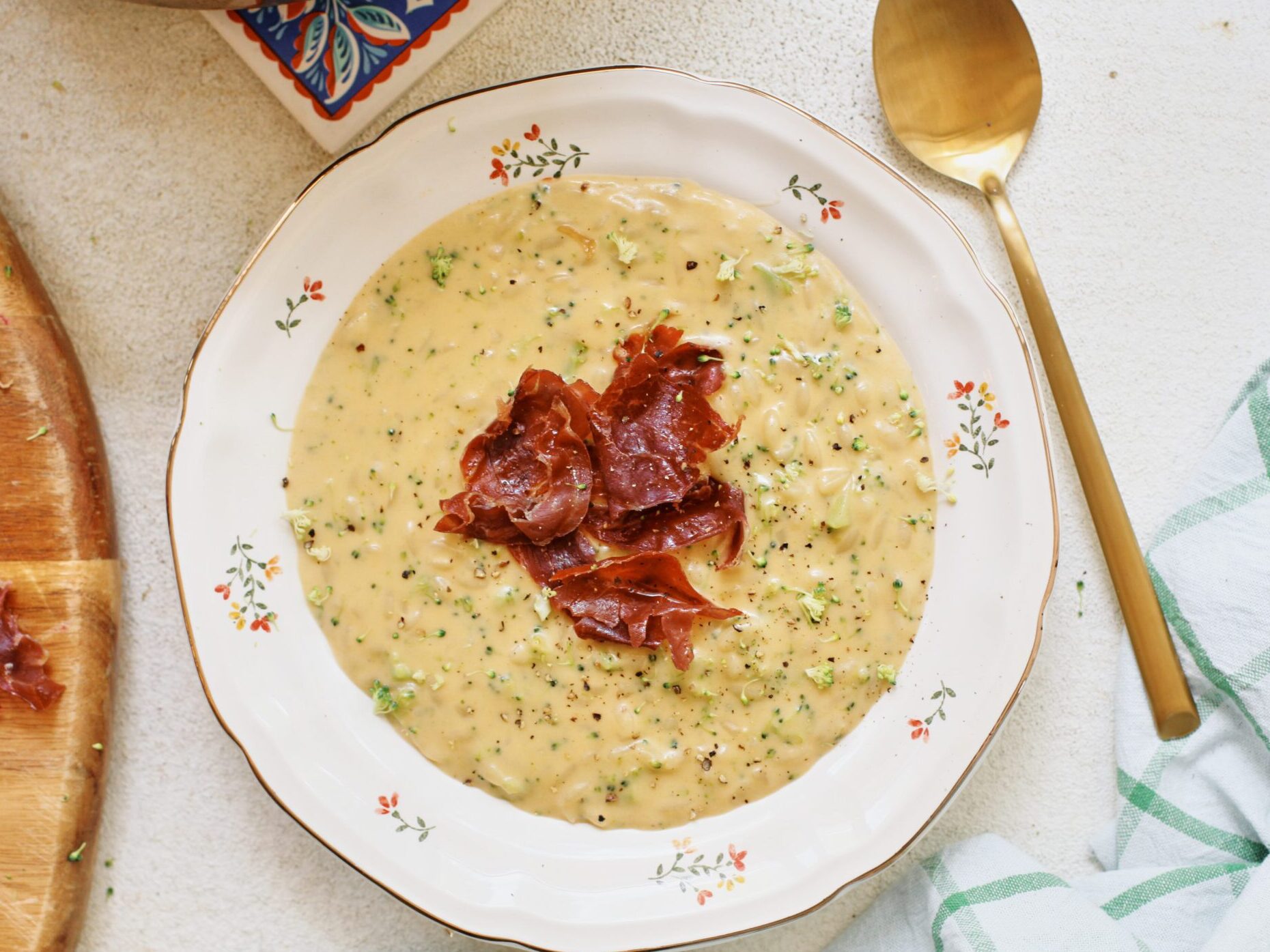 creamy broccoli cheddar orzo soup with crispy pancetta on top in a bowl