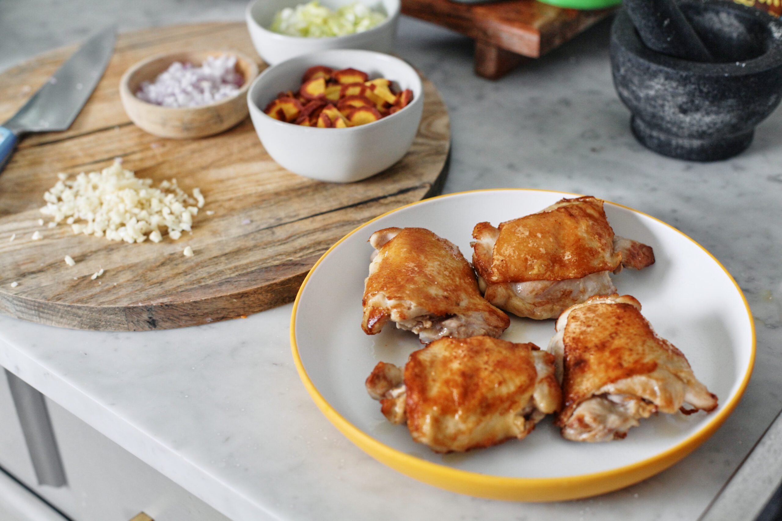 perfectly golden seared chicken thighs next to the mise en place ingredients about to go into the sillet