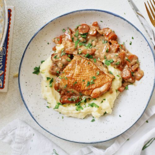 plated coq au vin blanc over a bed of creamy mashed potatoes with fresh Italian parsley on top