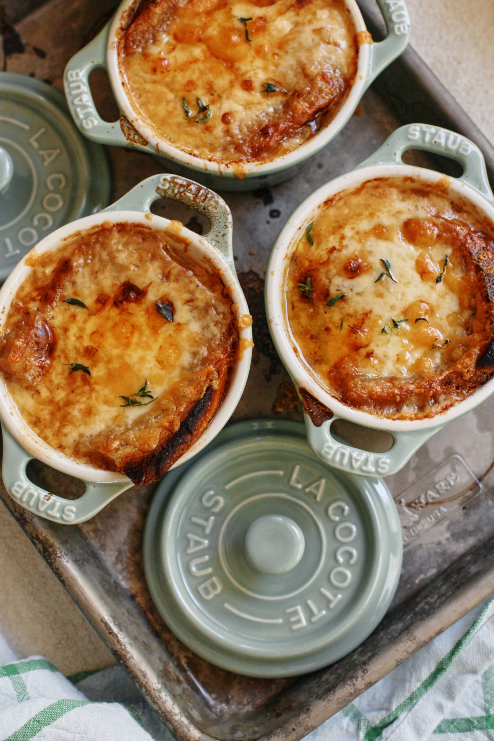 french onion soup in mini green dutch ovens that are arranged on a sheet pan, topped with golden, melted cheese