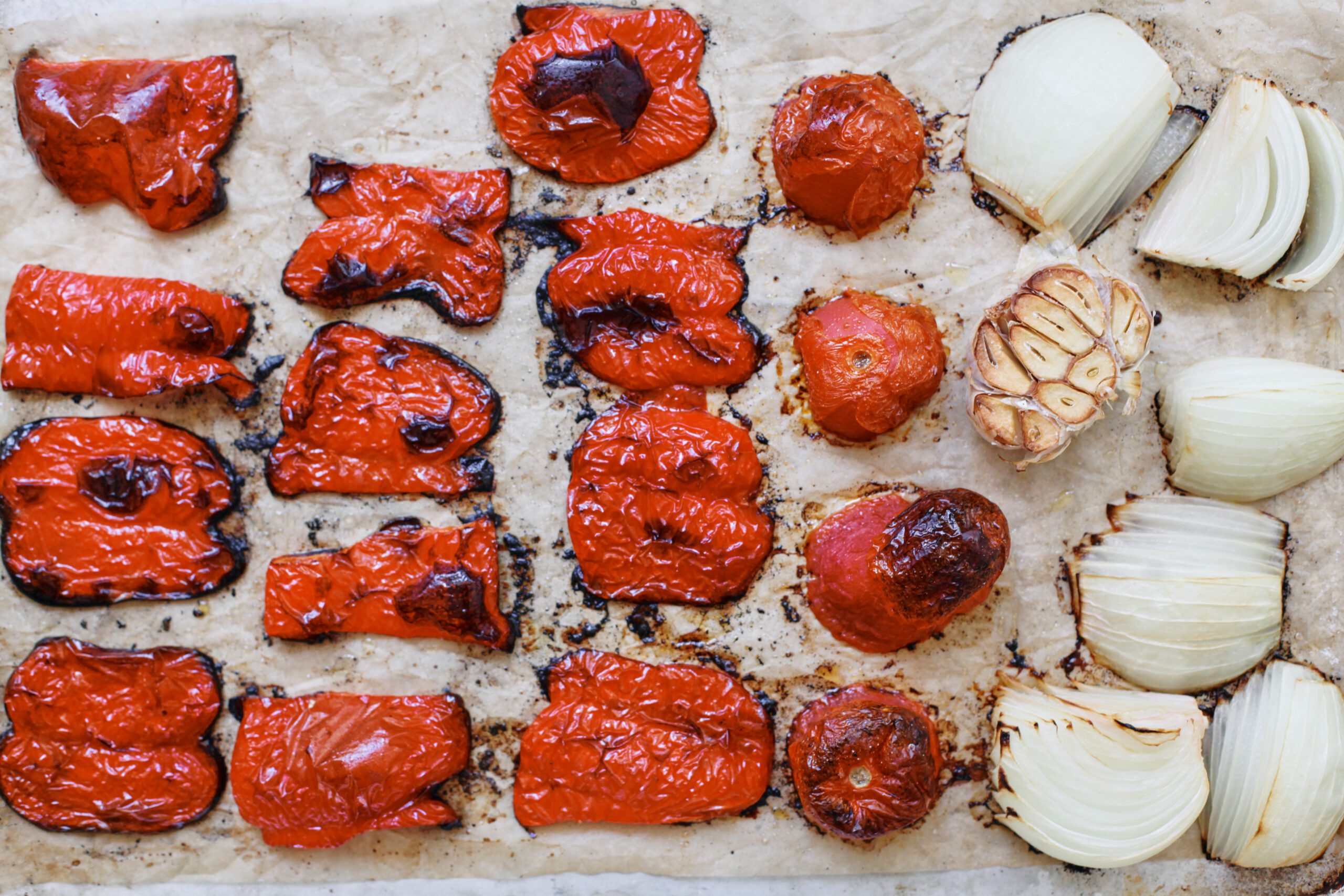 Italian Wedding Soup 3 red bell peppers, tomatoes, an onion, and a head of garlic arranged on a baking sheet and roasted