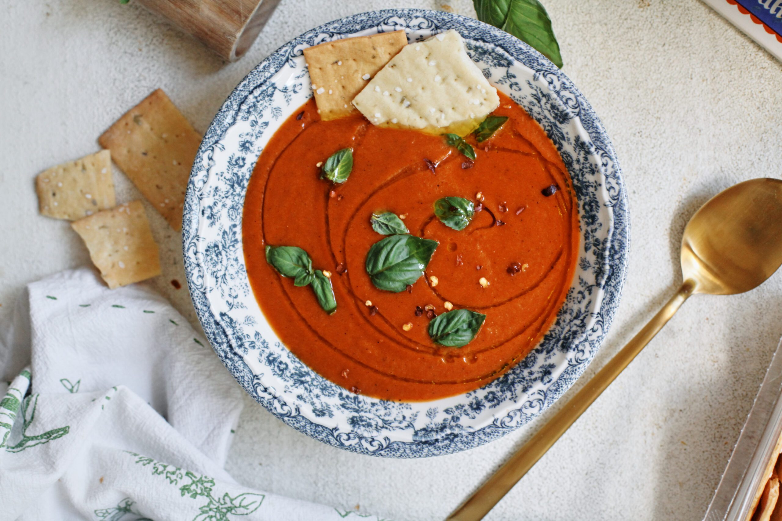 Roasted Red Pepper White Bean Soup 10 Roasted Red Pepper & White Bean Soup in a white bowl with a blue floral pattern, garnished with basil, olive oil, red pepper flakes, and Firehook Rosemary Sea Salt Crackers