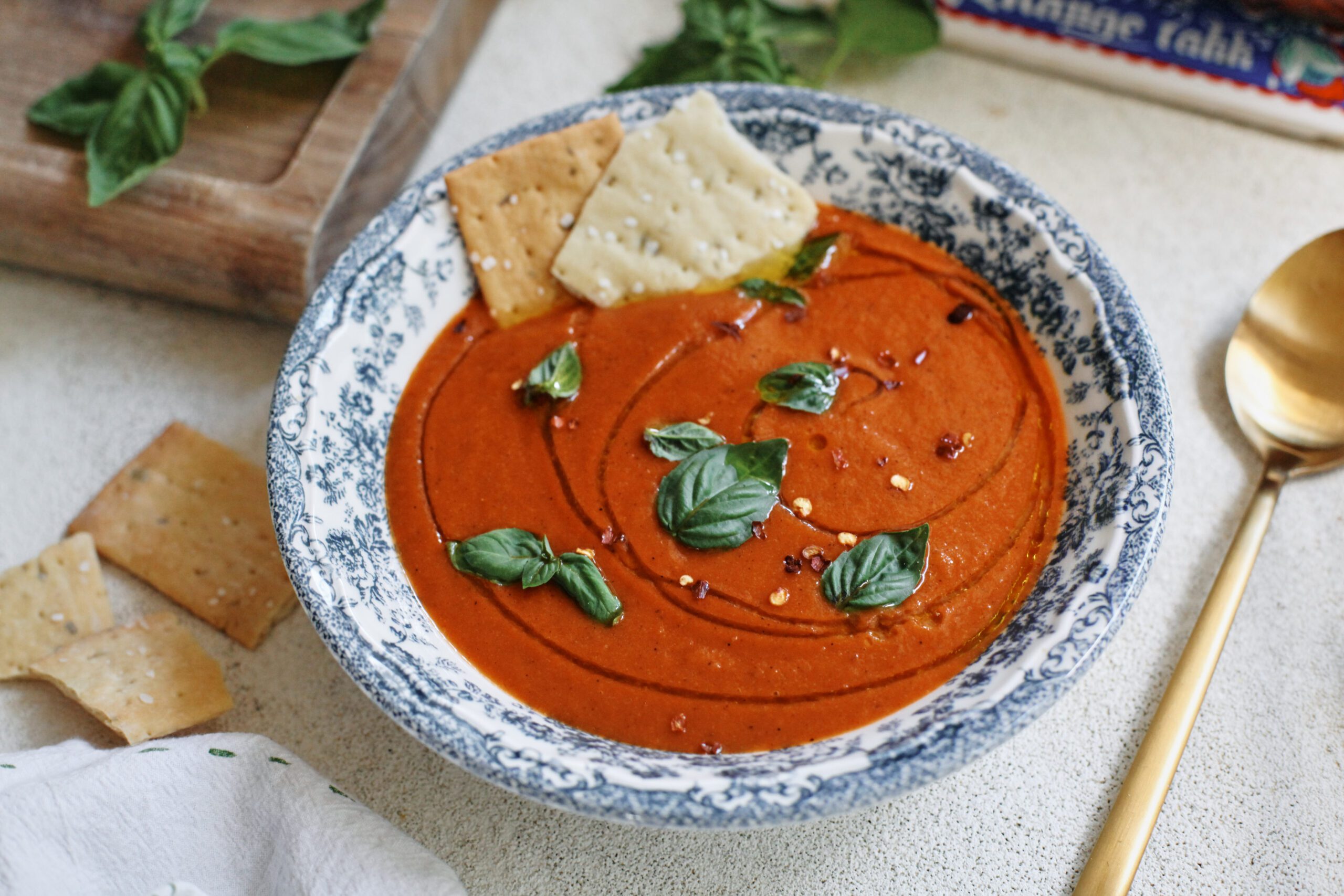 Roasted Red Pepper & White Bean Soup in a white bowl with a blue floral pattern, garnished with basil, olive oil, red pepper flakes, and Firehook Rosemary Sea Salt Crackers