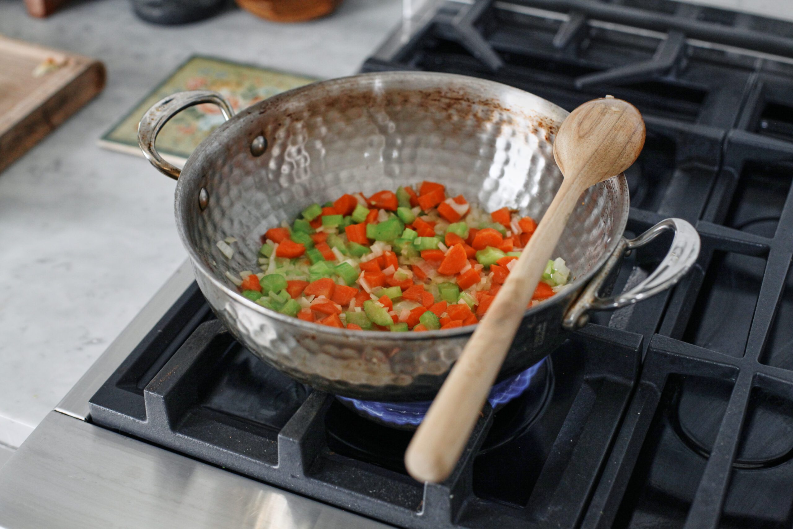 chopped carrots, celery, and onion sauteing in a pan with a wooden spoon resting on the pan