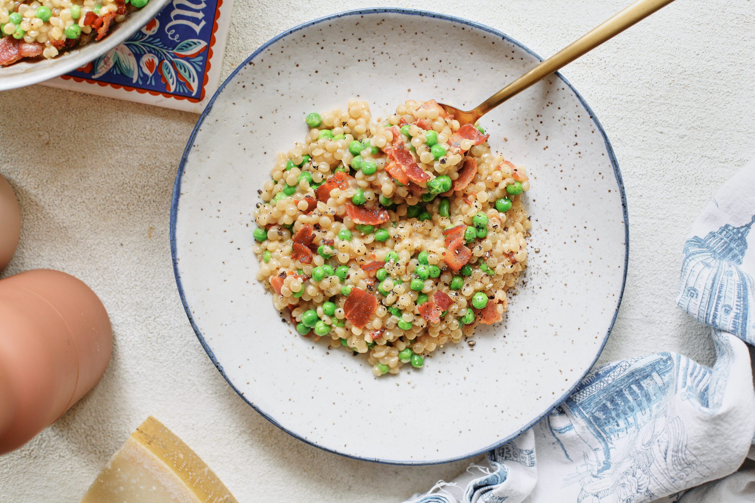 pearl couscous with bacon & peas served into a white bowl
