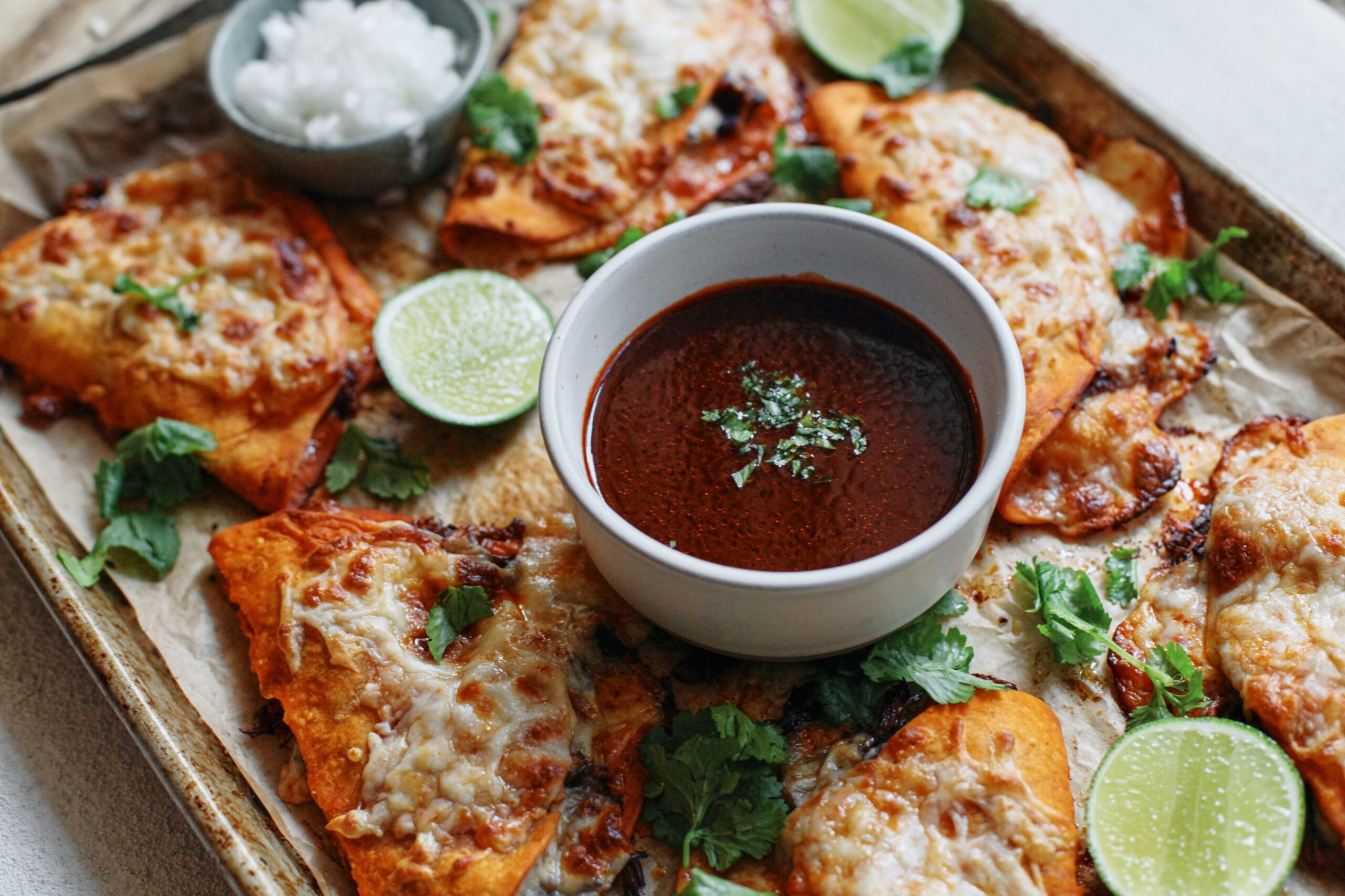 birria sheet pan tacos + a bowl of consomme dressed with cilantro, lime wedges, and a bowl of chopped white onions