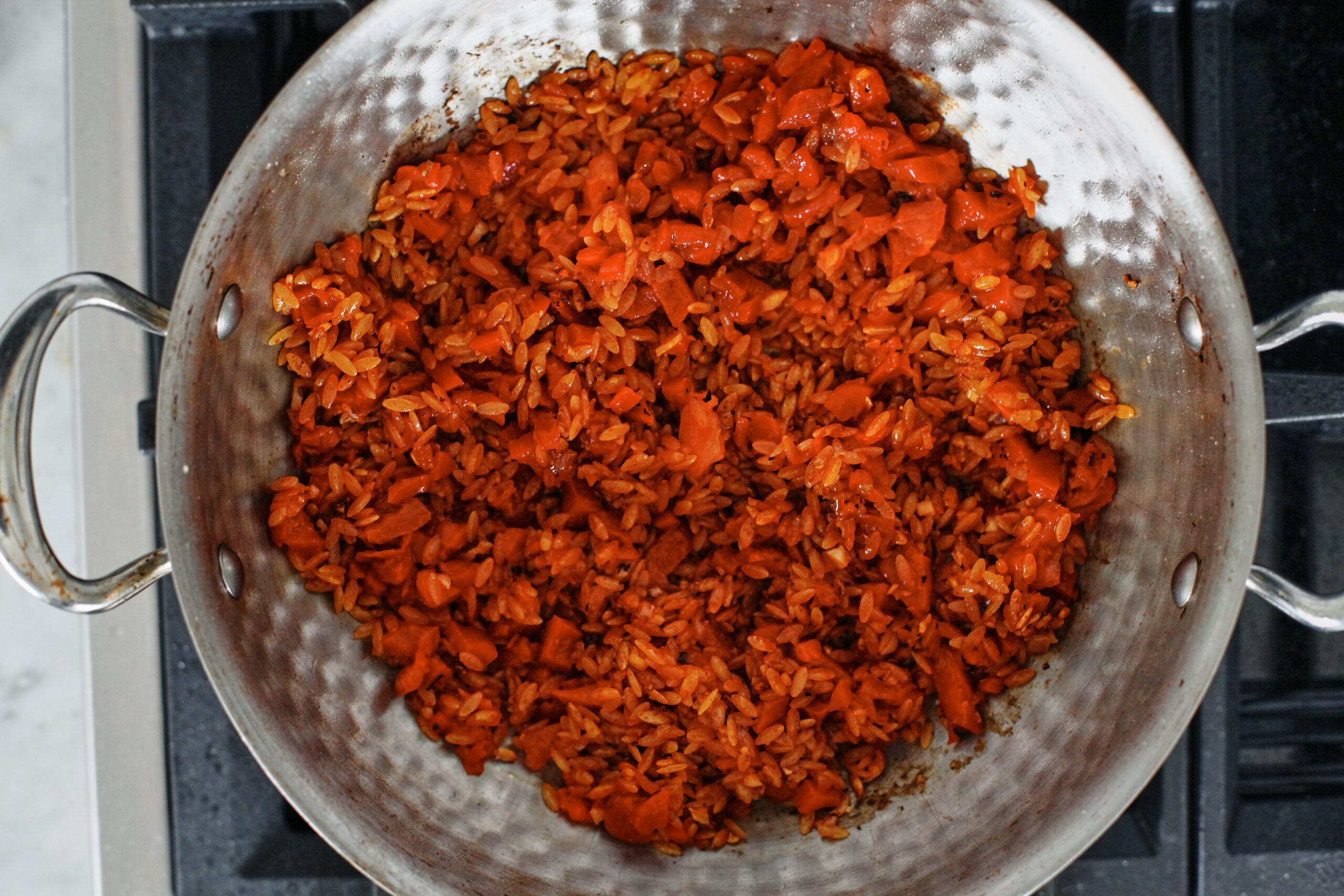 tomato paste and roasted red peppers stirred into the orzo in a large pan