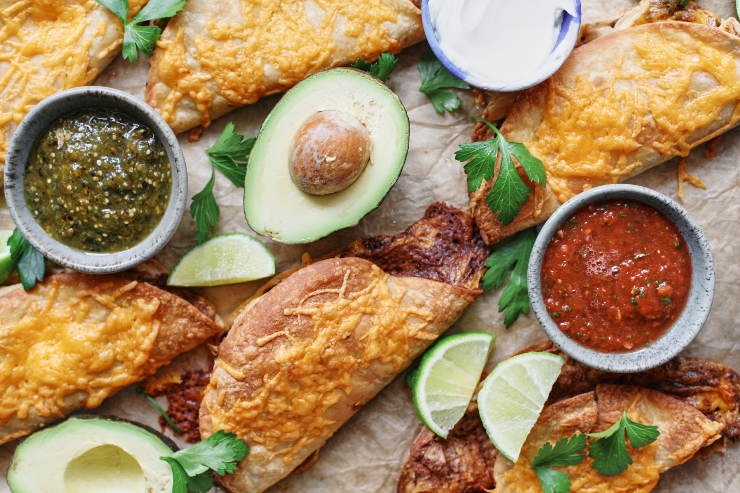 black bean sheet pan tacos arranged on a sheet pan with bowls of red and green salsa, lime wedges, a halved avocado, and cilantro