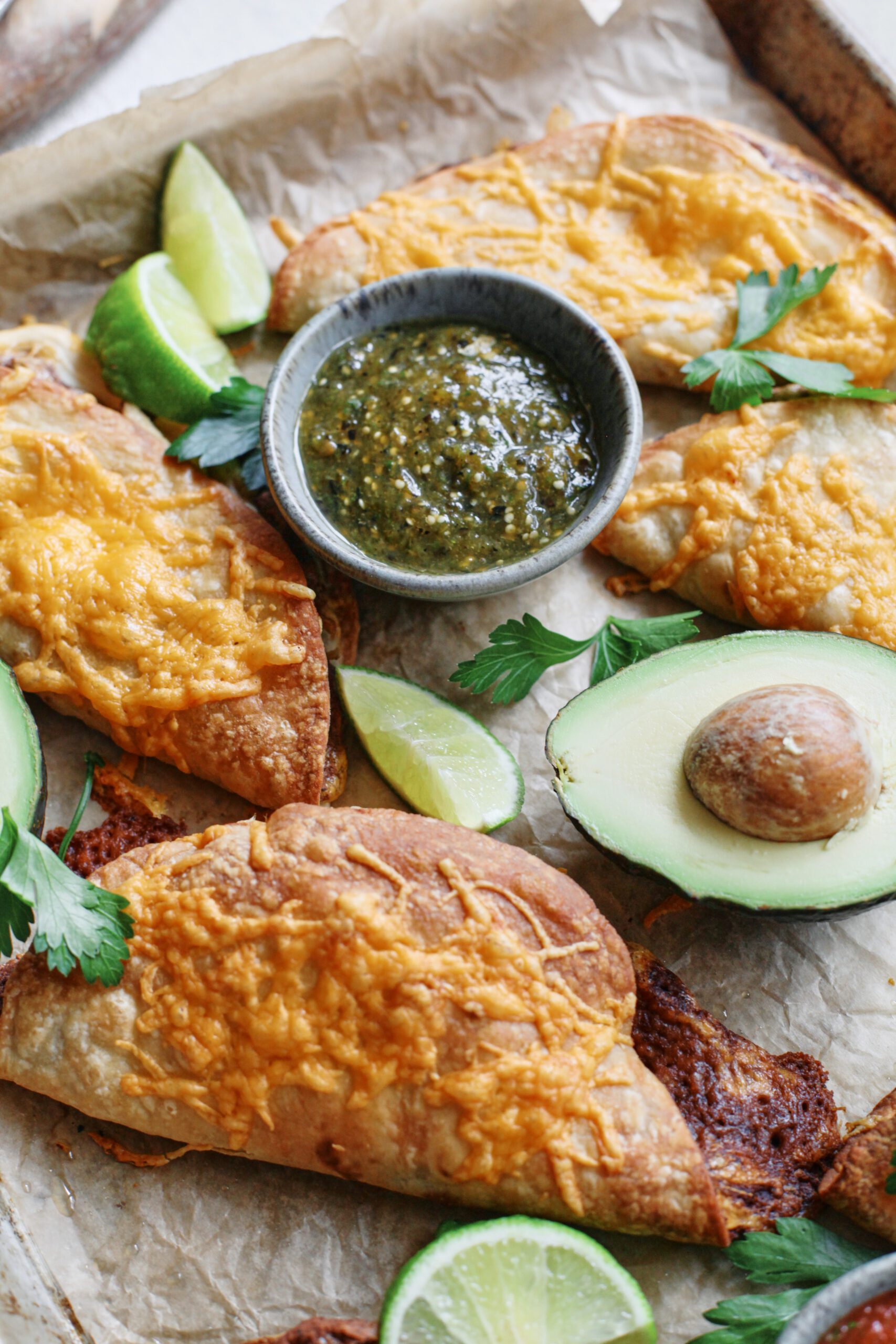 black bean sheet pan tacos arranged on a sheet pan with bowls of red and green salsa, lime wedges, a halved avocado, and cilantro