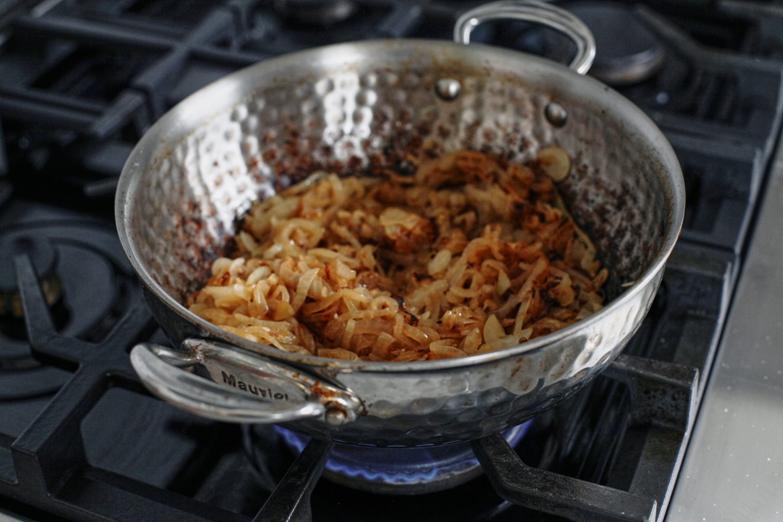 sliced onions caramelizing in a hammered steel pan on a gas range