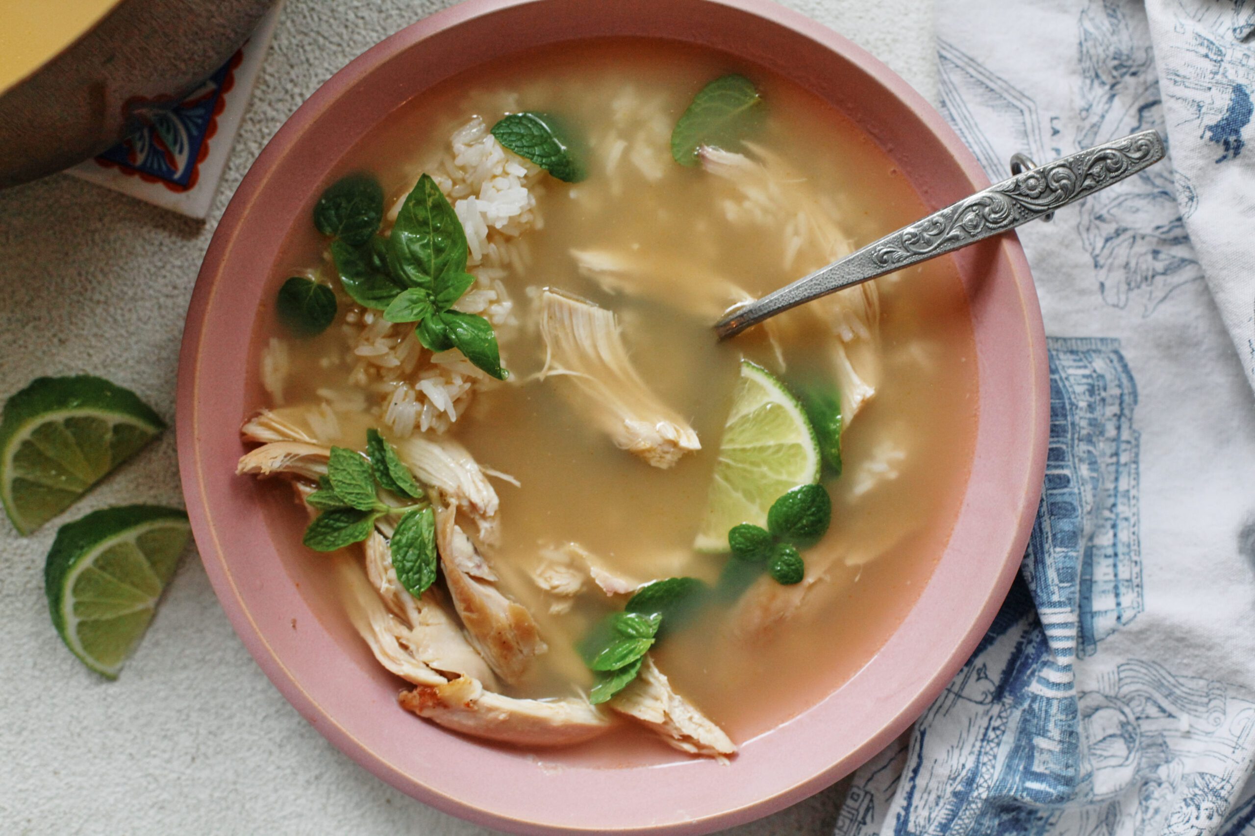 Overhead photo of a bowl of ginger chicken rice soup with shredded rotisserie chicken, fluffy white rice, and fresh mint and basil on top, garnished with a lime wedge