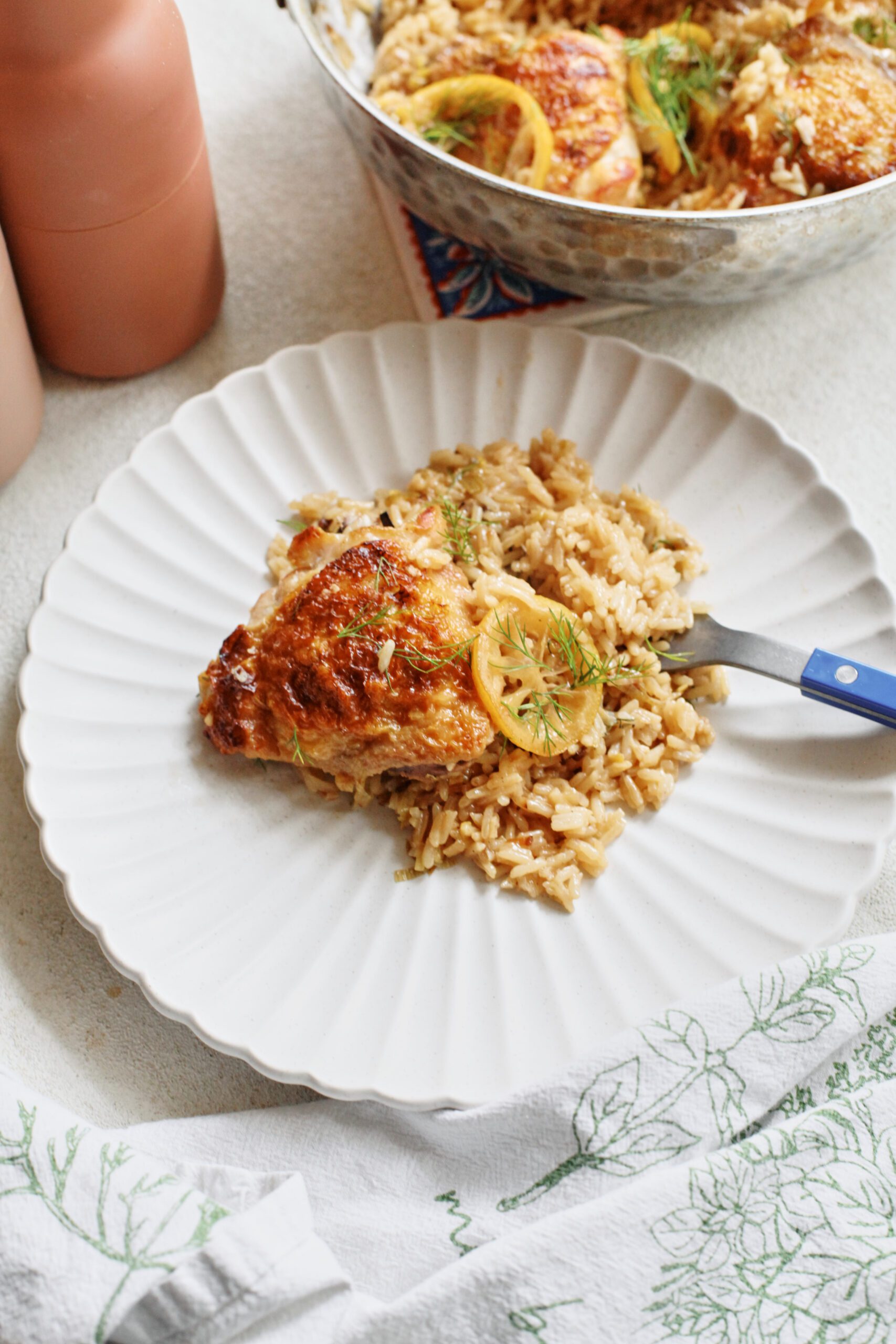 a chicken thigh served over rice, garnished with a seared lemon slice and fresh dill, served on a white plate with scalloped edges
