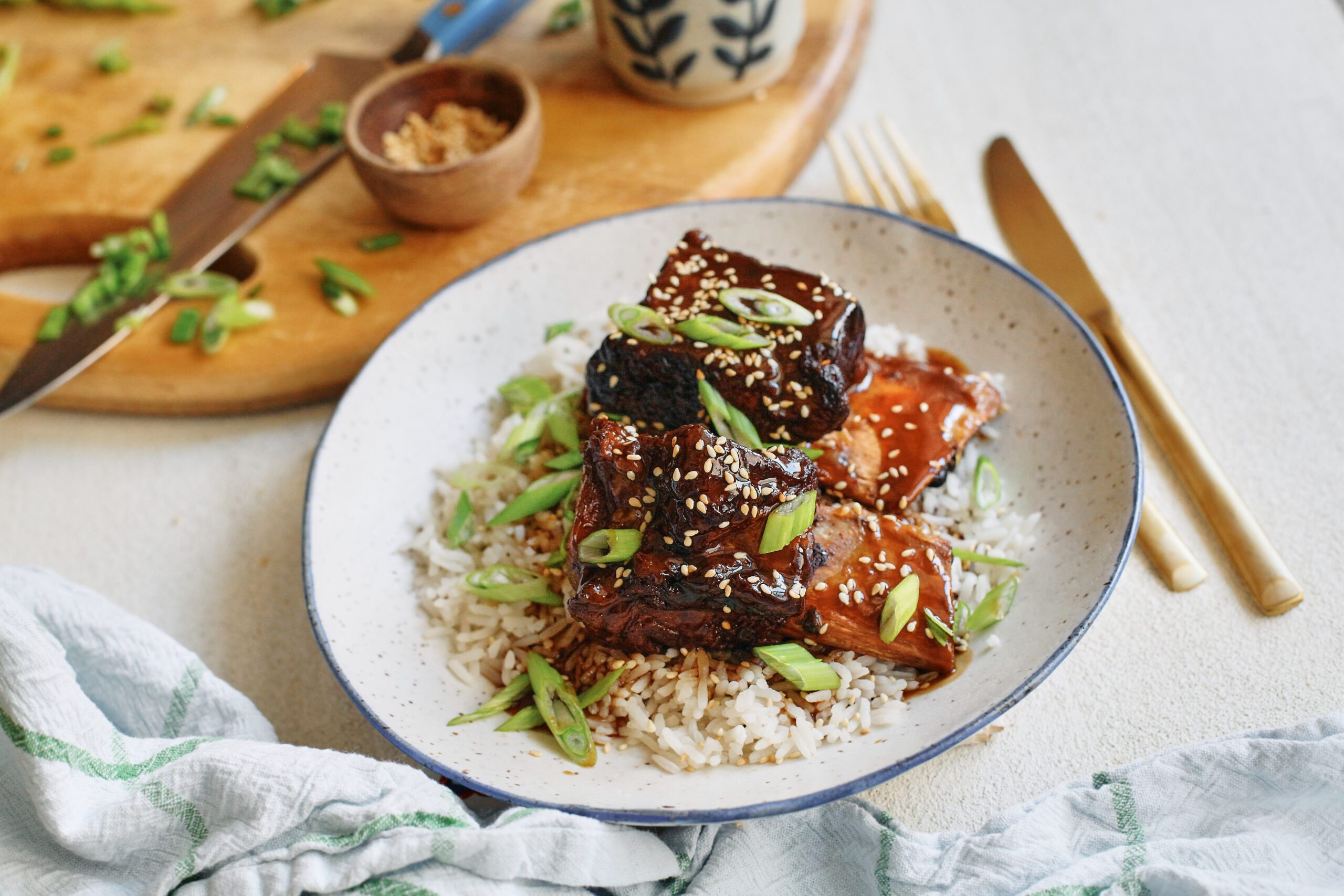 sticky soy and citrus short ribs over white rice, garnished with green onions and sesame seeds