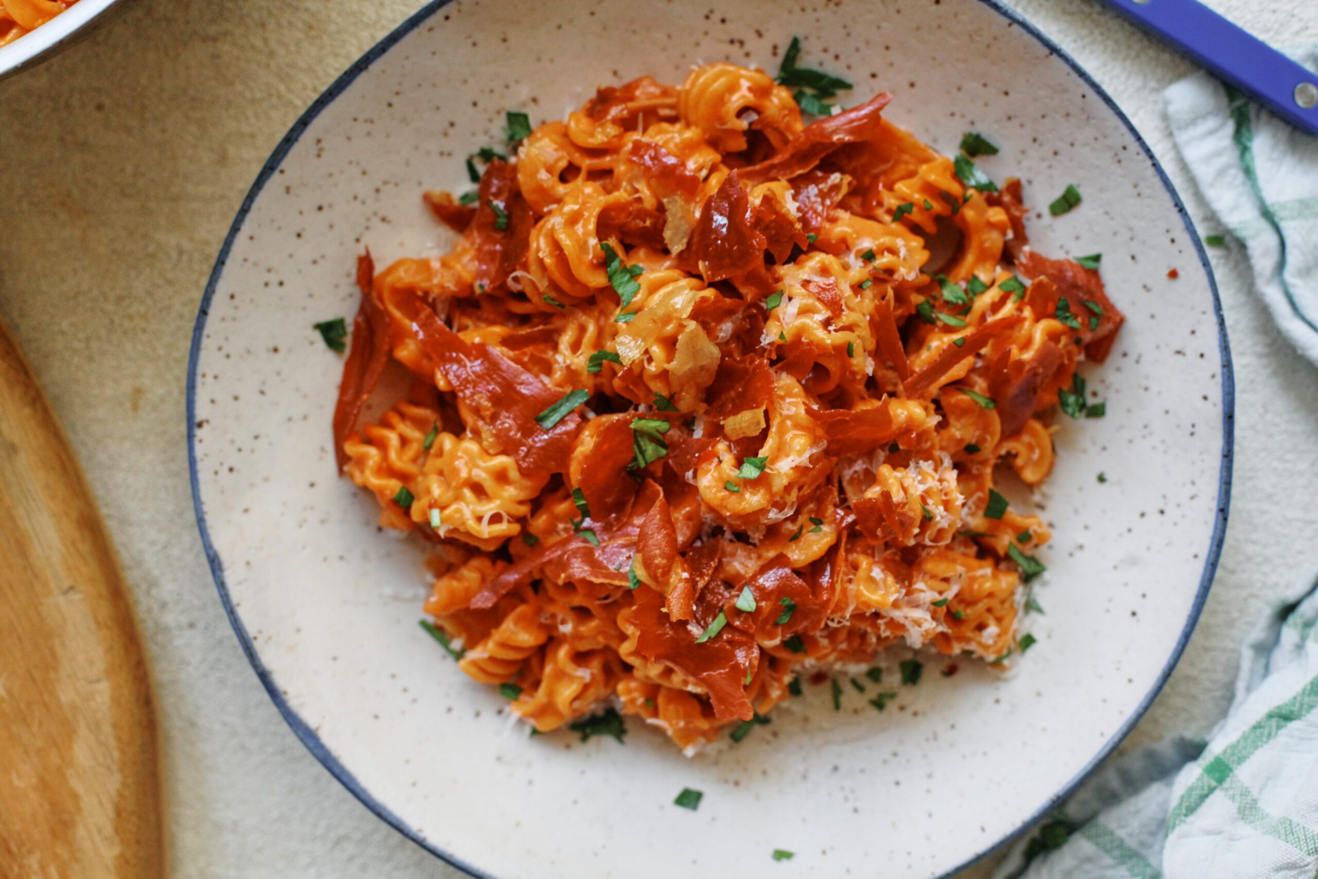 overhead photo of spicy vodka radiatore pasta with pieces crispy prosciutto and Italian parsley on top. It is in a white dish with a black rim