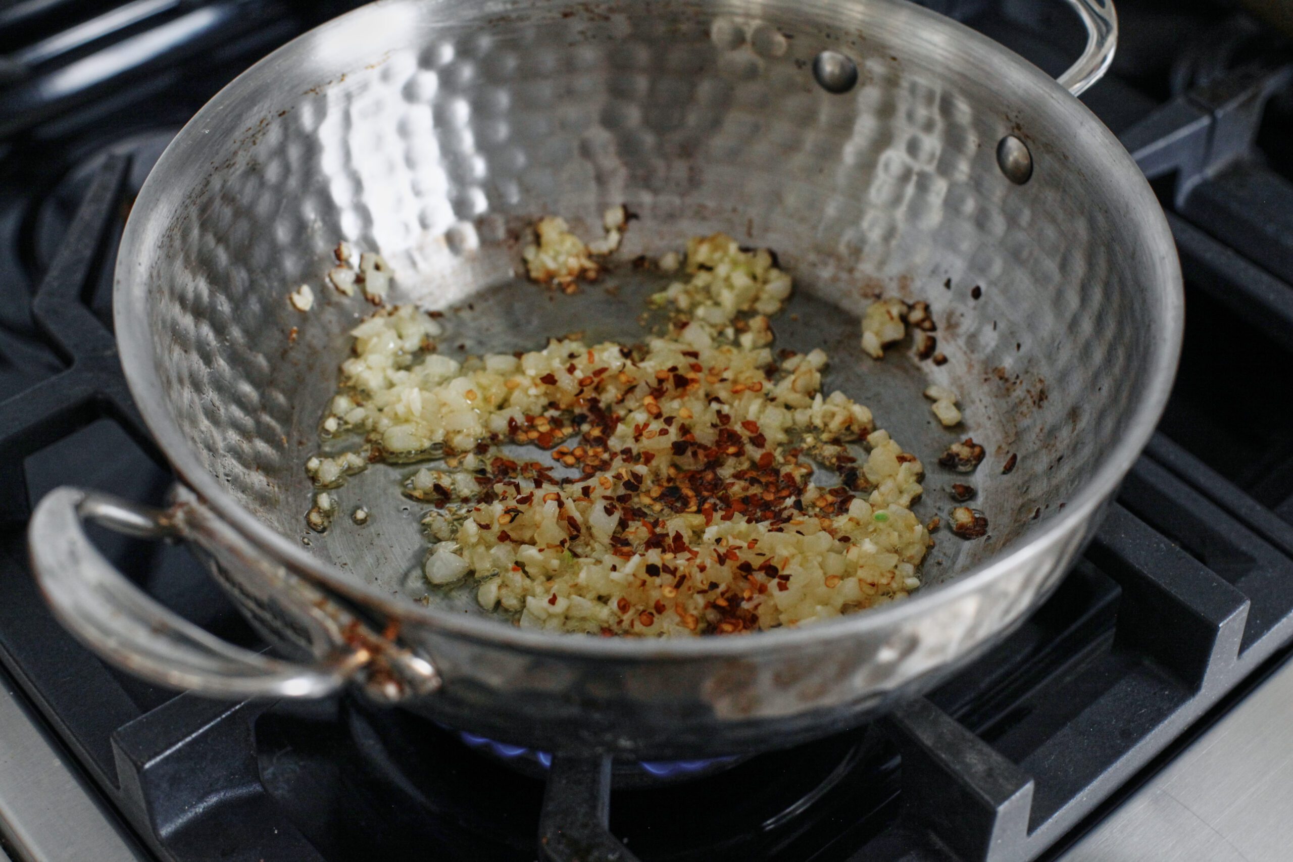 diced onion, minced garlic, and red pepper flakes sauteing in a hammered steel pan